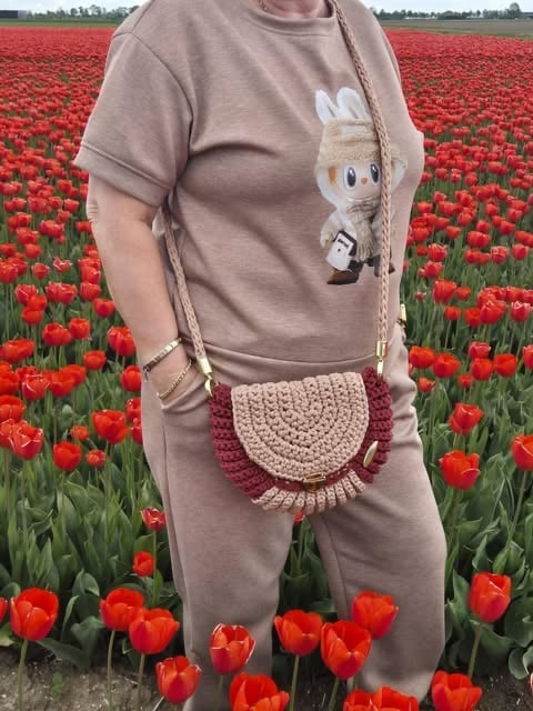 Person wearing beige outfit with bunny graphic and crochet bag standing in red tulip field