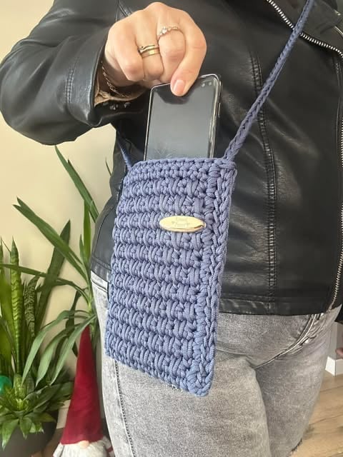 Person holding a phone in a periwinkle crocheted crossbody bag while wearing a black leather jacket