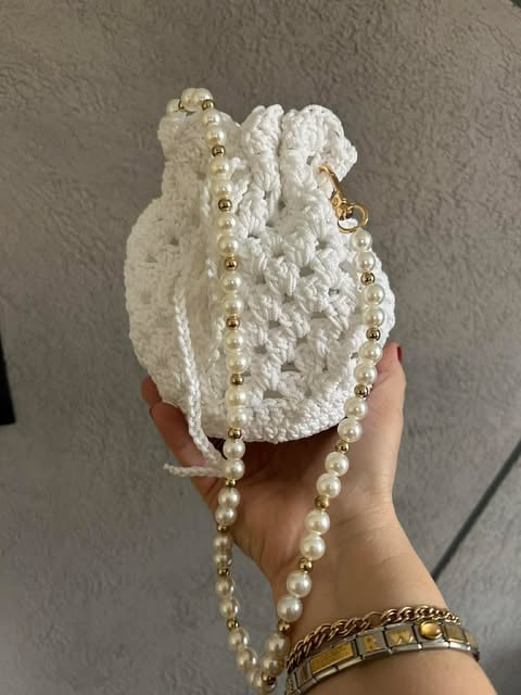Hand holding white crocheted pouch decorated with pearl and gold beaded strands and chain