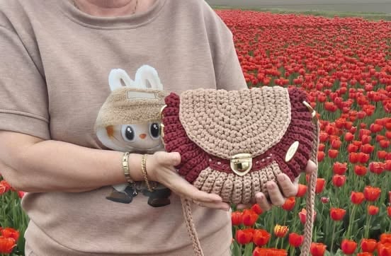 Person holding crocheted items in front of a red tulip field
