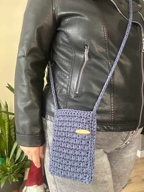 Person wearing gray leather jacket with small blue knitted crossbody bag with strap