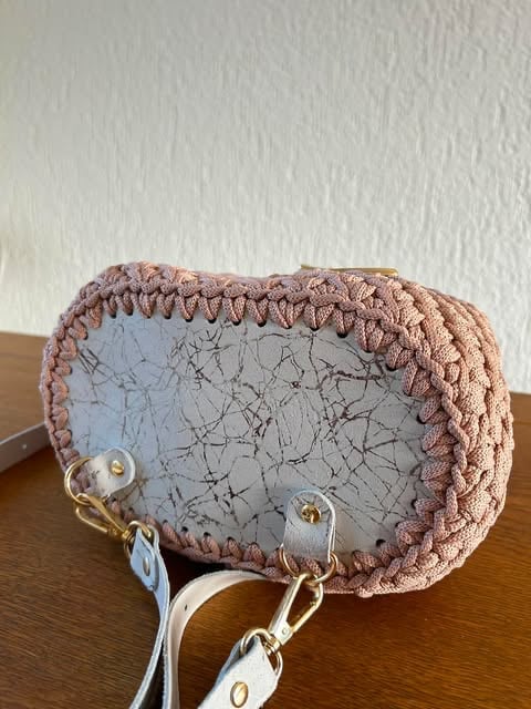 Pink knitted pouch with crackled blue-gray front panel and white strap attachment rings on wooden surface