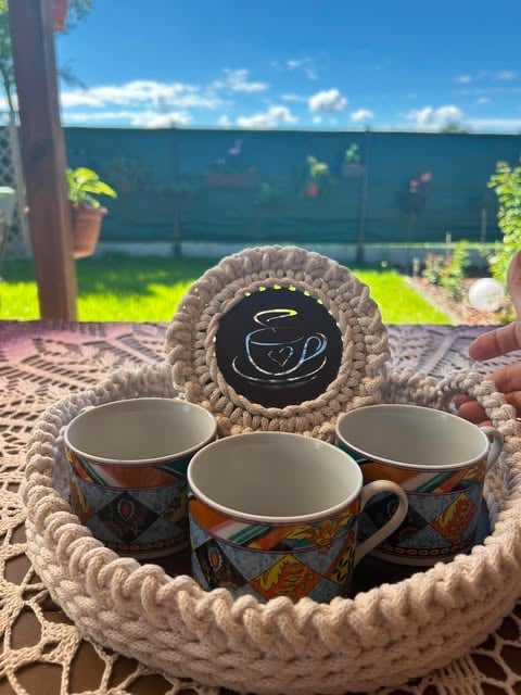 Three decorative mugs arranged in a rope circle with a chalkboard coffee cup sign, displayed outdoors on a sunny day