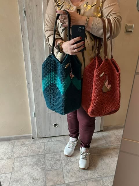 Person taking mirror selfie wearing tan cardigan, burgundy leggings, white sneakers, holding teal and red knit handbags