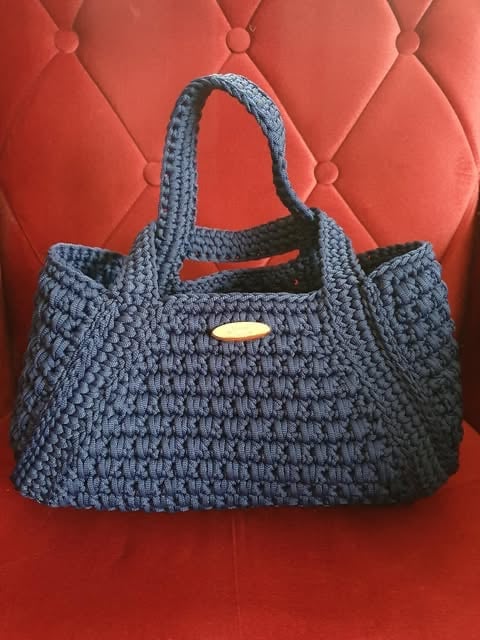 Navy blue quilted handbag with dual handles and gold plaque detail against red quilted background