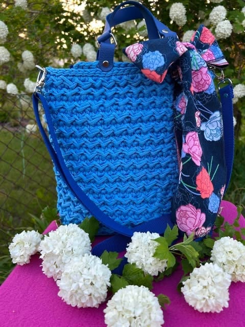 Blue quilted tote bag with colorful floral scarf surrounded by white hydrangeas and pink flowers