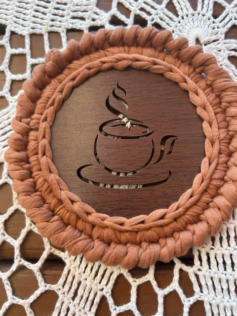 Circular wooden wall art with braided tan rope border featuring a steaming teapot and cup design, displayed on white macramé background