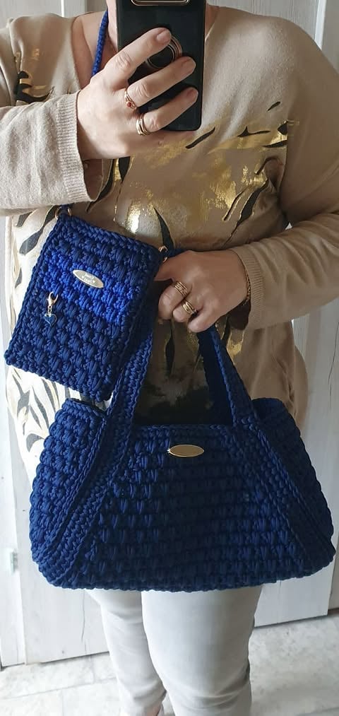 Person holding smartphone taking mirror selfie, wearing beige cardigan, gold pants, white tights, and displaying blue quilted handbag and matching crossbody bag